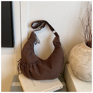 Detailed view of a brown plaid hobo bag with drawstring sides on a vintage book
