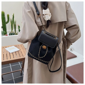 Detail of a black mini backpack featuring a gold chain strap and turn-lock closure on model