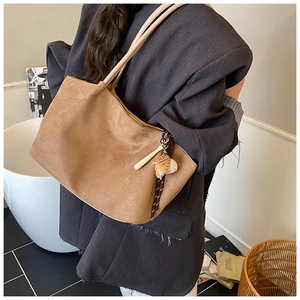 Detalle de bolso tote de ante marrón con un colgante de guante de béisbol y una pelota