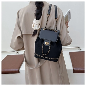 Detail view of black patchwork backpack with gold chain strap worn over a trench coat