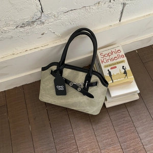 Detail view of green canvas handbag with black leather straps against a white brick wall