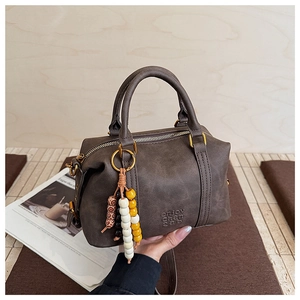 Detailed close-up of brown Boston bag with colorful beaded charm and embossed logo