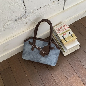 Close-up of grey-blue textured bag with brown leather handles and silver buckle details