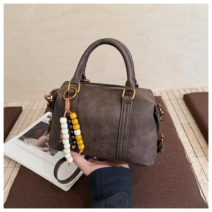 Detail of dark brown matte Boston bag featuring a branded logo and beaded charm detail