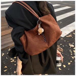 Detalle del bolso tote de ante marrón con colgante de béisbol en un entorno urbano