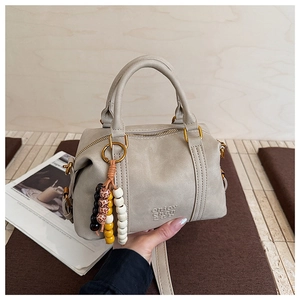Close-up of minimalist retro Boston bag with beaded tassel and embossed logo detail