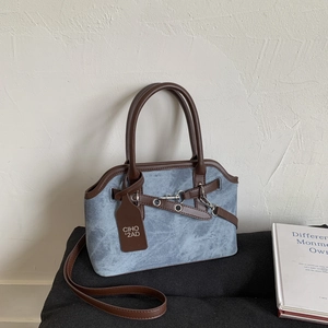 Detail of blue denim fabric crossbody bag with brown leather trim and metal buckle