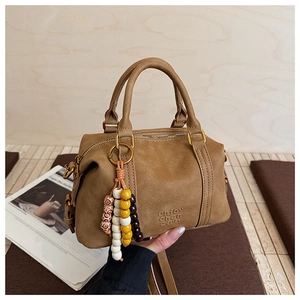 Detail of a brown suede pillow bag featuring a beaded tassel charm and embossed logo