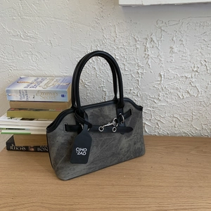 Detailed close-up of grey textured handbag with black round handle and silver metal eyelets
