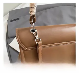 Close-up of silver metal swivel hook and braided shoulder strap on a brown leather bag