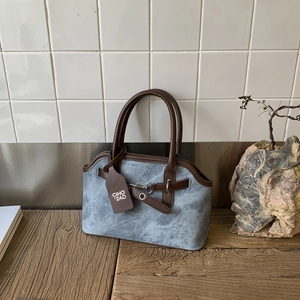 Detailed close-up of blue denim fabric handbag with brown leather trim and metal hardware