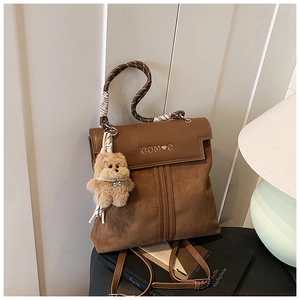 Detailed shot of dark brown mixed leather backpack with teddy bear charm on books