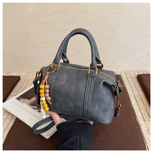 Close-up of grey matte Boston bag featuring embossed logo and colorful beaded charm