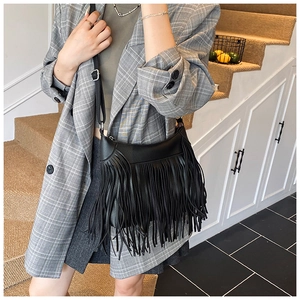 Détail d'un sac seau à franges noir porté par un mannequin en costume gris chic