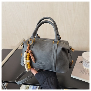 Close-up of gray frosted Boston bag with beaded pendant and gold zipper detail on rack