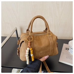 Detail of a brown suede Boston bag with gold hardware and beaded tassel charm