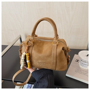 Detailed view of camel Boston bag with beaded charm and embossed brand lettering