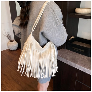 Detail view of a cream bucket bag with long tassels and thin faux leather strap on shoulder