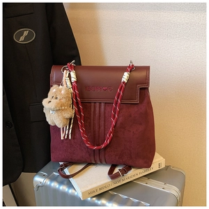 Close-up of wine red patchwork backpack with plush bear charm on silver luggage