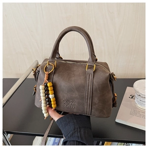 Detail of dark brown leather Boston bag with retro gold hardware and ethnic bead charm