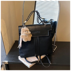 Close-up of black leather backpack with woven handle and plush dog pendant on display