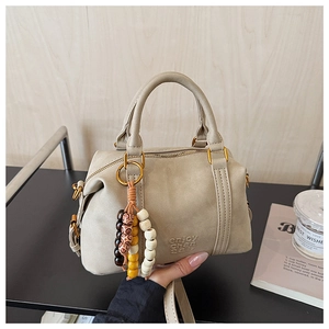 Close-up of matte beige Boston bag featuring embossed logo and colorful beaded tassel detail