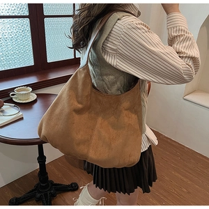 Close-up of a large brown suede hobo bag with vertical stitching in a cozy cafe setting
