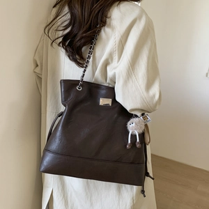 Détail d'un cabas en cuir marron foncé avec bandoulière chaîne et charm monstre poilu