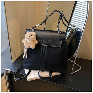 Detail of black backpack with woven handle, embossed logo and plush bear charm