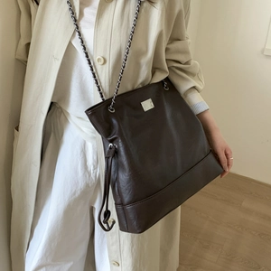 Détail d'un cabas vintage en cuir marron foncé avec chaîne argentée sur modèle