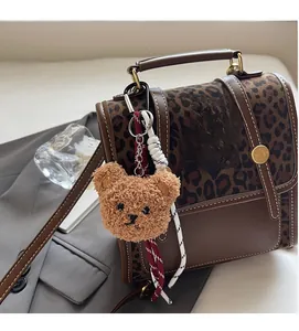 Detail of leopard print handbag featuring a plush bear charm and fashion logo nameplate