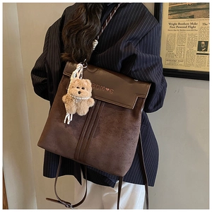 Detail view of retro brown patchwork backpack with bear charm and pearl necklace accessory