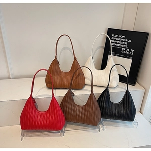 Cinque borse hobo intrecciate in rosso, marrone, bianco e nero esposte su piedistalli bianchi
