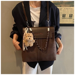Detail of dark brown vintage backpack with leather texture and plush bear pendant