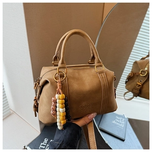 Close-up of brown suede pillow bag with embossed text and colorful beaded pendant detail