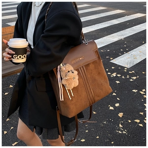 Detailed view of brown suede backpack with golden logo and cute plush bear accessory
