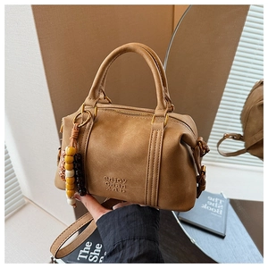 Detail of camel Boston bag with debossed logo, round handles and beaded charm accessory