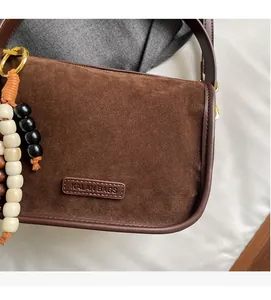 Close-up of soft brown faux suede shoulder bag with beaded charm and gold hardware detail