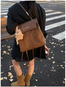 Retro brown flap backpack with plush bear charm detail on city street with ginkgo leaves
