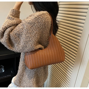 Dettaglio di una borsa hobo in pelle intrecciata marrone abbinata a un maglione di lana