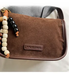 Detailed close-up of brown suede bag with KALAN BAGS logo and beaded tassel