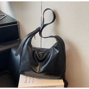 Detail of black glossy hobo bag with silver zipper and adjustable strap on book
