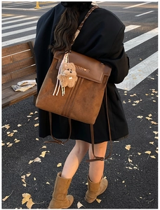 Brown vintage backpack with bear charm and golden logo shown in an autumn street scene