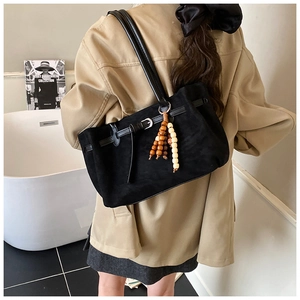 Detail of black suede tote bag with decorative strap and wooden bead charm on shoulder