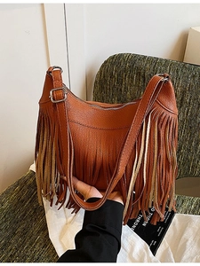 Sac seau marron à franges avec texture cuir grainé et bandoulière sur une chaise