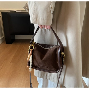 Gros plan détaillé d'un sac en daim marron foncé avec ferrures dorées et breloque en perles