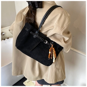 Detail of black suede tote bag with leather strap and decorative wooden bead charm