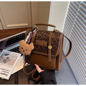 Detail of dark brown leopard print backpack with plush bear charm and fashion label