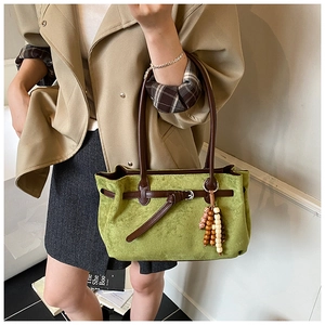 Detail of green suede tote bag featuring brown leather handles and beaded tassel charm