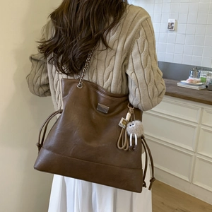 Détail d'un grand sac cabas vintage marron avec un charme en peluche et bandoulière chaîne